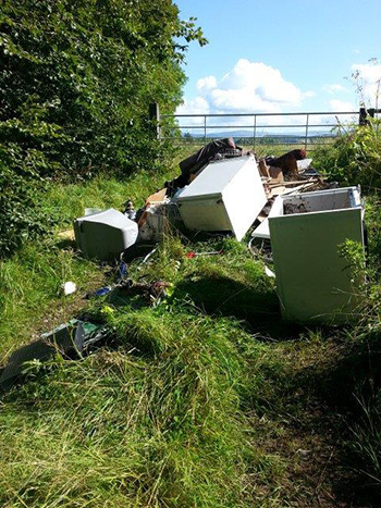 Fly-tipping on highway verge, blocking entrance to field.
